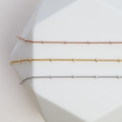 a rose gold bead chain necklace, a gold bead chain necklace and a silver bead chain necklace laid out together on a white background